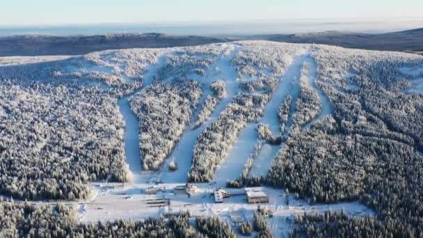 Vista de la base de esquí moderna y pistas de esquí rodeadas de bosque en invierno contra el cielo azul. Filmación. Vista aérea — Vídeos de Stock