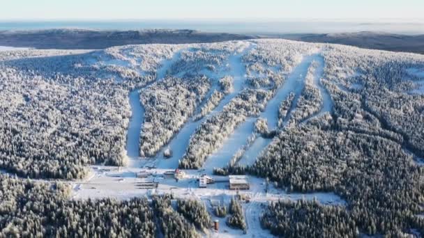 Vista de la base de esquí moderna y pistas de esquí rodeadas de bosque en invierno contra el cielo azul. Filmación. Vista aérea — Vídeos de Stock