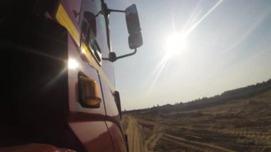 Yan görünüm kırmızı kamyon taksi yeşil ağaçlar devam tozlu asfaltsız kırsal yolda devam edelim. Büyük kamyon ülke, bulutlu gökyüzü arka plan, tozlu yolda sürme bir tekerlek görünümünden.