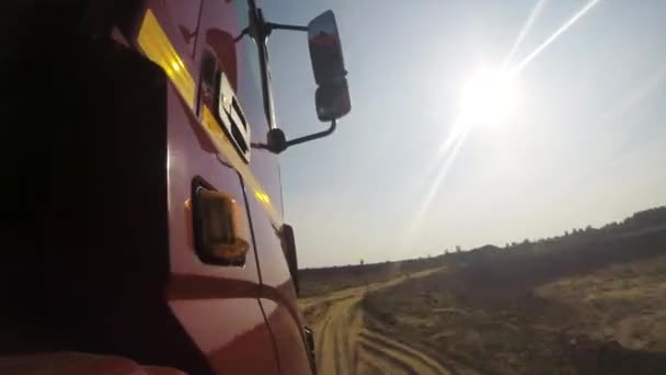 Visa från ett hjul av off-road truck ridning i en grusväg på molnig himmel bakgrund. Scen. Stäng för röda hytten på en lastbil som flyttar på landet, dammig väg i en sommar, solig dag. — Stockvideo