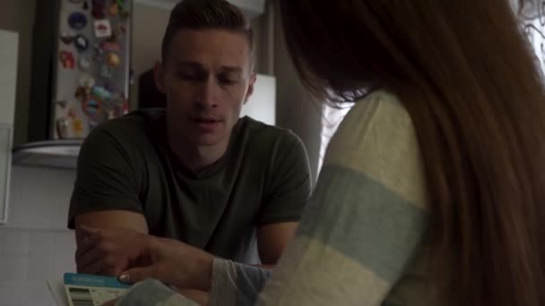 Worried couple reading together a letter standing near the table in the kitchen. Nervous man touching his mouth while his girlfriend opens a letter and begins to read. — Stock Video