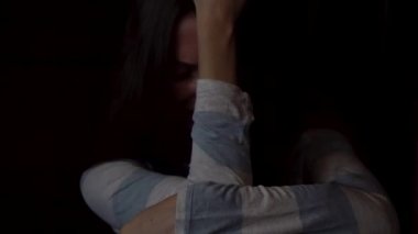 Dizlerinin sarılma ve koyu arka plan üzerinde yalnızlık kavramı ağlayan üzgün, genç bir kadın portresi. Depresif kadın tek başına oturmak ve karanlık duvara ağlama.