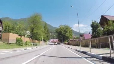 Araba ön camın güneşli Europe kasaba, yeşil ağaçlar, dağlar mavi gökyüzü karşı yoldan görünümünü. Sahne. Yoldan hareketli bir araç, sürücü görünümü içinde arasında evlerin doğal görünümü.