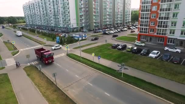 Aéreo para caminhão dirigindo na rua da cidade entre casas e calçadas. Cena. Camião grande e vermelho a mover-se na encruzilhada da cidade num dia ensolarado de verão . — Vídeo de Stock