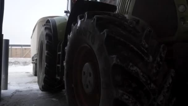 Primer plano para pasar al tractor de garaje con remolque en la granja en invierno, concepto de agricultura. Filmación. Maquinaria agrícola, conducción de tractores sobre nieve . — Vídeo de stock