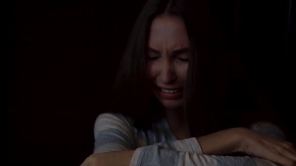 Portret van een droevige, jonge vrouw haar knieën knuffelen en huilen op donkere achtergrond, eenzaamheid concept. Depressief vrouwelijke zitten alleen en huilen tegen de donkere muur. — Stockvideo