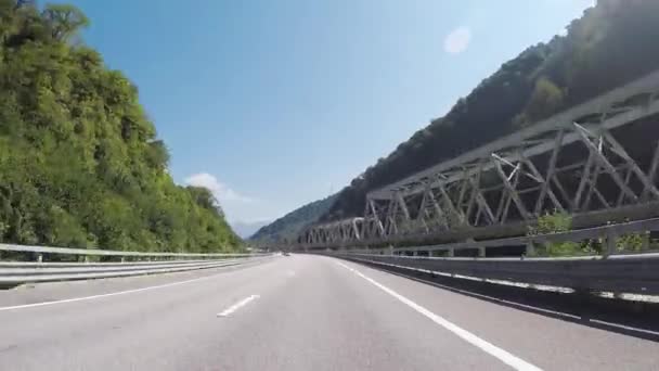 Vue sur la route depuis le pare-brise de la voiture en Europe ensoleillée, de nombreux arbres verts, des montagnes contre le ciel bleu. Scène. Vue panoramique de la nature estivale de l'intérieur d'un véhicule en mouvement, vue du conducteur . — Video