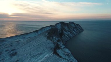 Hava görünümünü kapsadığı karanlık deniz suyu bulutlu gökyüzü karşı karda güneş doğarken bir kayalık cape üzerinde. Güzel deniz manzara