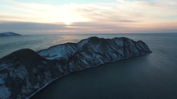 Vista aérea sobre un cabo rocoso cubierto de nieve en el agua oscura del mar contra el cielo nublado al amanecer. Le dispararon. Hermoso paisaje marino . — Vídeo de stock