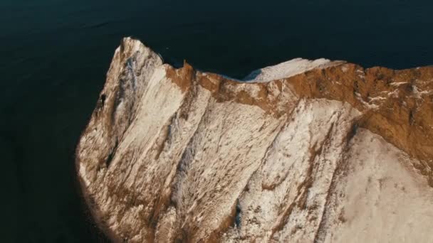 Vista aérea de la ladera marrón de la montaña cubierta de nieve cerca del mar con agua azul oscura. Le dispararon. Hermoso paisaje — Vídeos de Stock