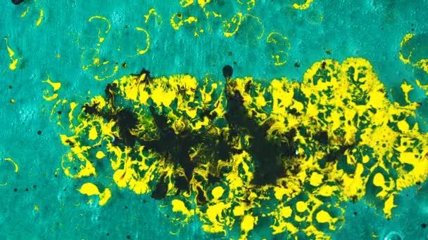 Primo piano della macchia di inchiostro giallo e gocce di inchiostro nero che cadono su uno sfondo di gel turchese. Arte e texture . — Video Stock