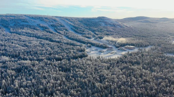 Vista superior de la base de esquí con pistas en la montaña. Filmación. Panorama de montañas cubiertas de nieve con pistas de esquí y recreación entre bosques de coníferas en día claro de invierno — Foto de Stock