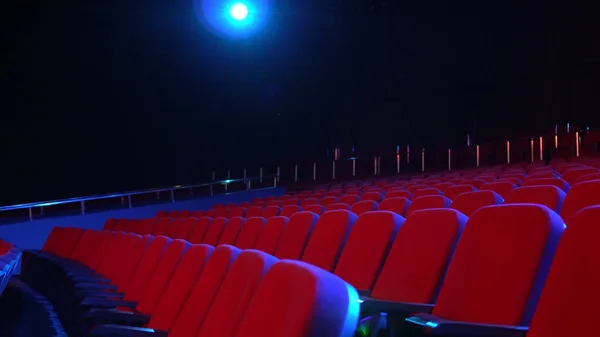 Filas vacías de asientos en la sala de cine. Cine vacío con asientos rojos en habitación oscura con proyector de luz en el fondo — Foto de Stock