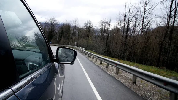 Car rides on mountain winding road. Side mirror of car driving along winding mountain road reflects trees and cloudy sky
