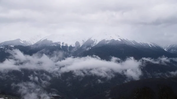 Vista superior del paisaje de montaña y pequeño complejo de invierno. Nubes sombrías que se ciernen sobre los picos de las montañas y las estribaciones del complejo invernal en clima nevado — Foto de Stock