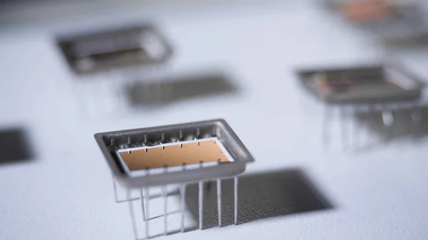 Close-up of microchip on legs. Electronic microchip with reflecting bronze surface on legs is on table with falling shadow