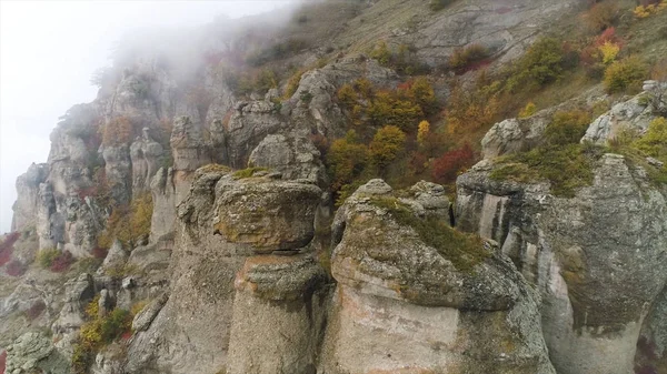 Stenen van ongebruikelijke vormen op de berg bedekt met wolken mist. Schot. Luchtfoto voor mistige dag in de bergen en de mooie vorm stenen met geel, herfst bomen en struiken. — Stockfoto