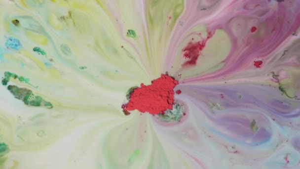 Color powder paint is mixed in water. Close-up of red powder in middle absorbs colorful washouts on surface of milk — Stock Video