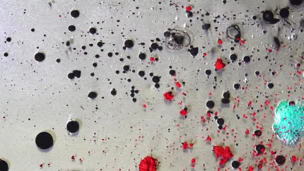 On surface of liquid drops of paint. Transparent thick liquid with ink droplets and scattered grains of paint — Stock Video