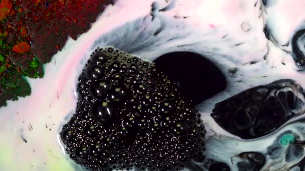 Close-up of bubbling black ink. On colorful surface of milk with paint stains appears bubbly black ink. Bubbling black oil stains contaminate colorful liquid — Stock Video