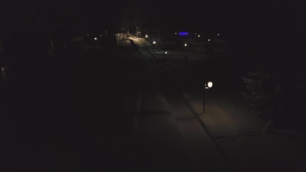 City street with snow-covered path illuminated by lanterns at night. Clip. Beautiful night darkness with light lanterns illuminating footpath near houses in winter — Stock Video