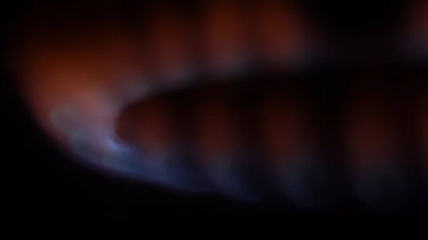 Närbild på brinnande spis eld i mörkret. Närbild av arbetande gasbrännare med svag brand i kök i mörkret — Stockfoto