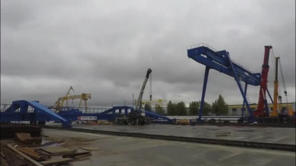 Gruas de pórtico grandes na empresa de transporte logístico em fundo cinza, céu nublado. Guindastes de pórtico, guindastes de caminhão e pessoas que executam trabalhos de carga, lapso de tempo . — Vídeo de Stock