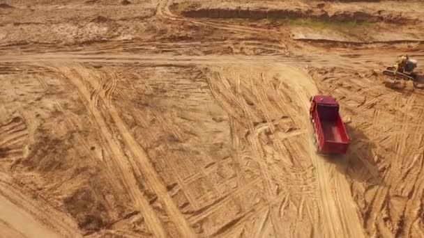 Vista del grande camion rosso vuoto che si muove su una pista sabbiosa vicino all'escavatore giallo nel deserto o nelle dune. Bella vista dall'alto . — Video Stock