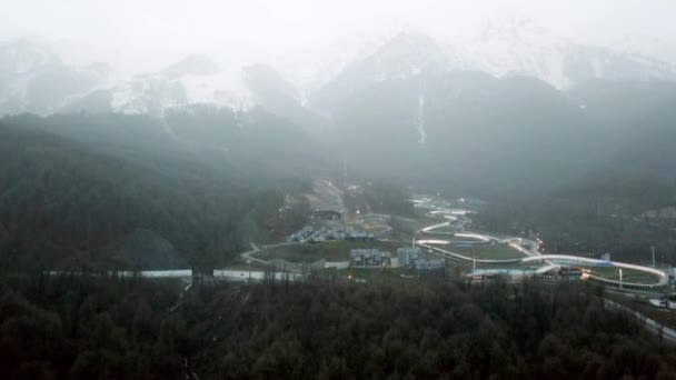 Resort vid foten av bergen i molnigt väder. Natursköna ovanifrån av berglandskap med snöiga toppar i dimma och liten resort på foten — Stockvideo