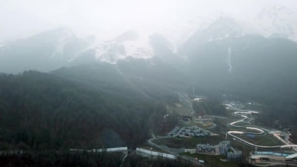 Resort au pied des montagnes par temps nuageux. Vue panoramique sur le paysage montagneux avec des sommets enneigés dans le brouillard et petite station balnéaire à pied — Video