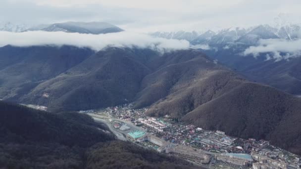 山の谷の下町風景の平面図です。霧の中で雪に覆われた山頂と麓森林面積の狭い谷の町の山脈の美しいパノラマの風景 — ストック動画