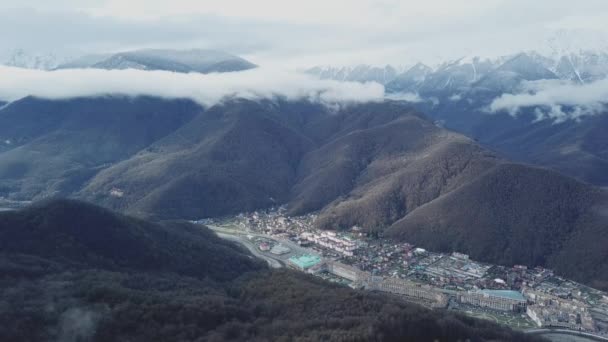 山の谷の下町風景の平面図です。霧の中で雪に覆われた山頂と麓森林面積の狭い谷の町の山脈の美しいパノラマの風景 — ストック動画