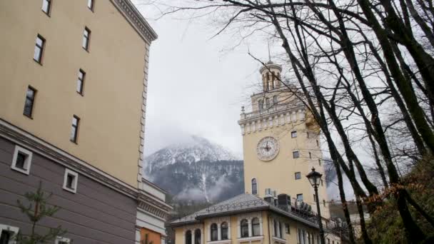 Курортный городок и горные снежные вершины. Аллея курортного города с видом на часовую башню и горы на заднем плане — стоковое видео