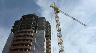 Alt görünümü yüksek bina sarı vinç yakınındaki bitmemiş inşaat mavi, bulutlu gökyüzü arka plan üzerinde. Bir yaz, güneşli günde metal vinç yakınındaki yapım aşamasında bina yüksek doğmak.