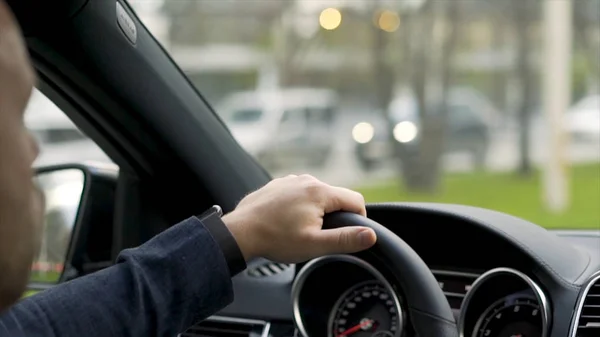 Hombre conduciendo coche desde la vista trasera en la calle de la ciudad a lo largo de los árboles verdes callejón. Acciones. Hombre de camisa gris con reloj negro coche de conducción en la carretera, interior del coche moderno . — Foto de Stock