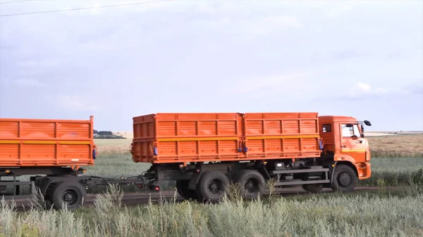 Orange, new ruck with trailer moving on country road on green and yellow field background. Scene. Lorry with a trailer in a countryside against cloudy sky. — Stock Photo, Image