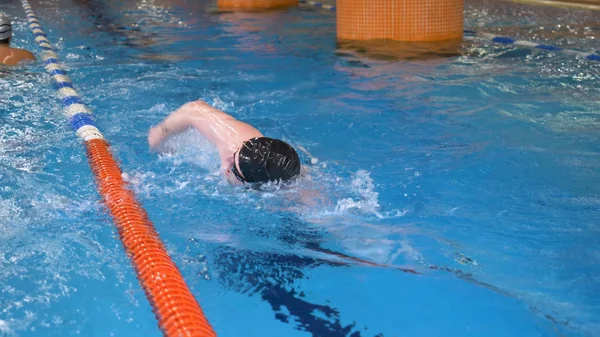 Joven hombre con gafas y gorra nadando en el agua azul de la piscina, interior. Deportista nada en aguas cristalinas de la piscina, estilo crawl, concepto de salud . —  Fotos de Stock