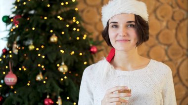 Santa Claus şapka ve şampanya oturma odası ve Noel ağacı arka plan, parti, içecekler, kutlama ve insanlar kavramı üzerinde Genç, güzel bir kadın. Bir şekilde dekore edilmiş Ladin üzerinde duran kadın.