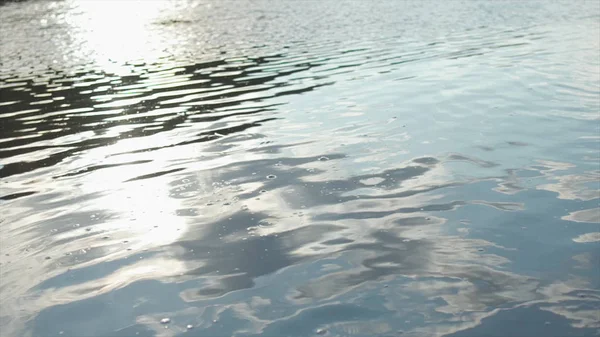 Primer plano de ondulaciones en la superficie del río con reflejos de nubes en el agua. Acciones. Flujo de agua oscura en río tranquilo con cielo y sol reflejados . —  Fotos de Stock