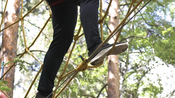 Primer plano para el hombre en el sendero de cuerda alta en el parque de aventura forestal, concepto de deporte al aire libre extremo. Acciones. Hombre en zapatillas negras caminando por la selva camino de la cuerda . —  Fotos de Stock