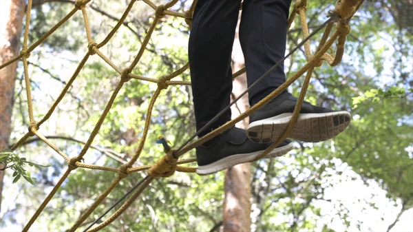 Close up para o homem em trilha de corda alta no parque de aventura florestal, conceito de esporte ao ar livre extremo. Estoque. Homem de tênis preto andando na selva corda maneira . — Fotografia de Stock