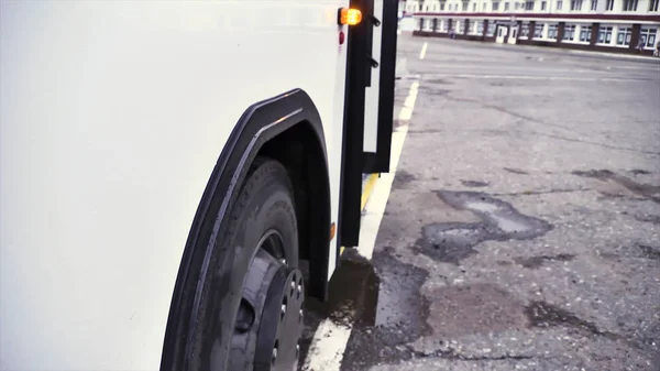 灰色のアスファルトの背景にドアとバスのホイールを開くと白いバスの側面図です。シーン。旅客バス、開かれたドアの点滅ライトとそのホイール、商業輸送ホイール概念のクローズ アップ. — ストック写真