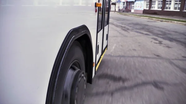 Вид збоку на білий автобус з відкритими дверима та колесом автобуса на сірому фоні асфальту. Сцена. Крупним планом пасажирський автобус, відкриті двері блимають світлом і його колесом, концепція комерційних транспортних коліс . — стокове фото