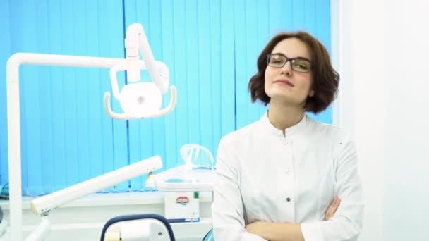 Güzel genç kadın diş hekimi ayakta silah portresi diş Kliniği kabine geçti. Gözlük kamera, tıp kavramı düz seyir emin doktor. — Stok video