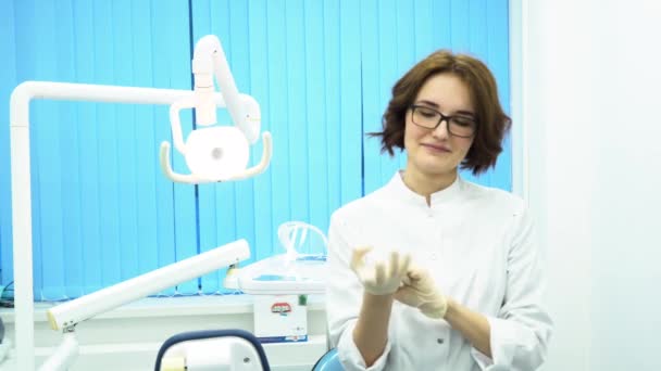 Ritratto di una giovane e bella dottoressa che indossa guanti medici. Assistente dentale femminile in occhiali indossare guanti in gabinetto dentale . — Video Stock