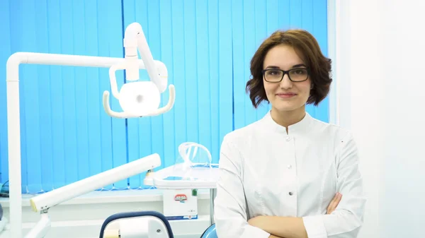 Retrato de una hermosa mujer joven dentista de pie brazos cruzados en el gabinete de la clínica dental. Médico de confianza en gafas mirando directamente a la cámara, concepto de medicina . —  Fotos de Stock