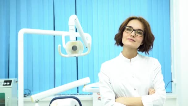Portrét krásná mladá žena zubař postavení zbraní přešel v zubní klinice kabinetu. Jistý lékař v brýlích dívá přímo do kamery, koncepce medicína. — Stock video