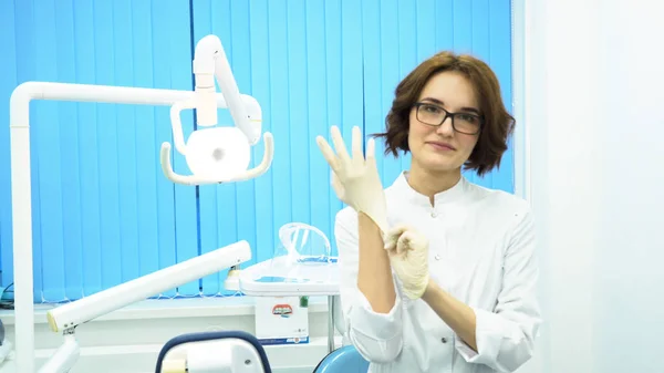 Portret van een mooie, jonge vrouw arts medische handschoenen. Vrouwelijke tandartsassistente in glazen handschoenen in tandheelkundige kast te zetten. — Stockfoto