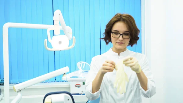 Portret van een mooie, jonge vrouw arts medische handschoenen. Vrouwelijke tandartsassistente in glazen handschoenen in tandheelkundige kast te zetten. — Stockfoto