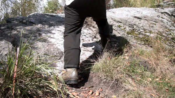 Κοντινό πλάνο της άνθρωπος λαστιχένιες μπότες ενώ πεζοπορία στο μονοπάτι στο βουνό στο μαραμένο χορτάρι. Τα πόδια ο άνθρωπος πεζοπόρος αναρρίχηση η απότομη πλαγιά του βράχου. — Φωτογραφία Αρχείου